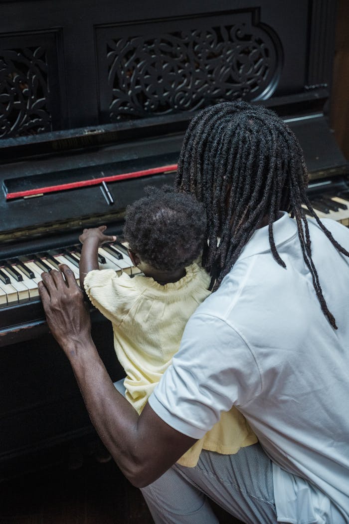 A father teaching his daughter to play the piano, captured from a vertical angle indoors.