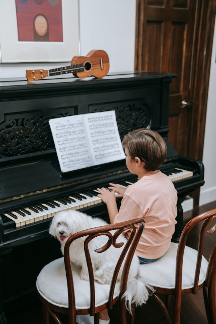 A young boy sitting at a piano with sheet music, accompanied by his dog, indoors.