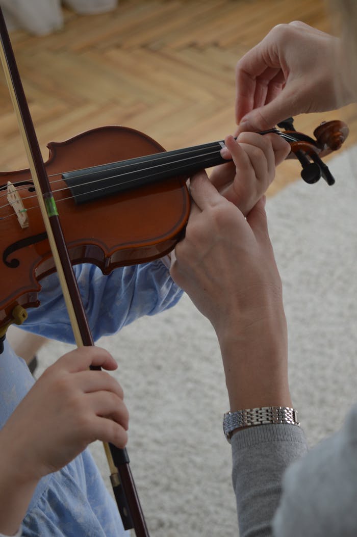 A child receives violin lessons from a teacher, focusing on hand positioning.
