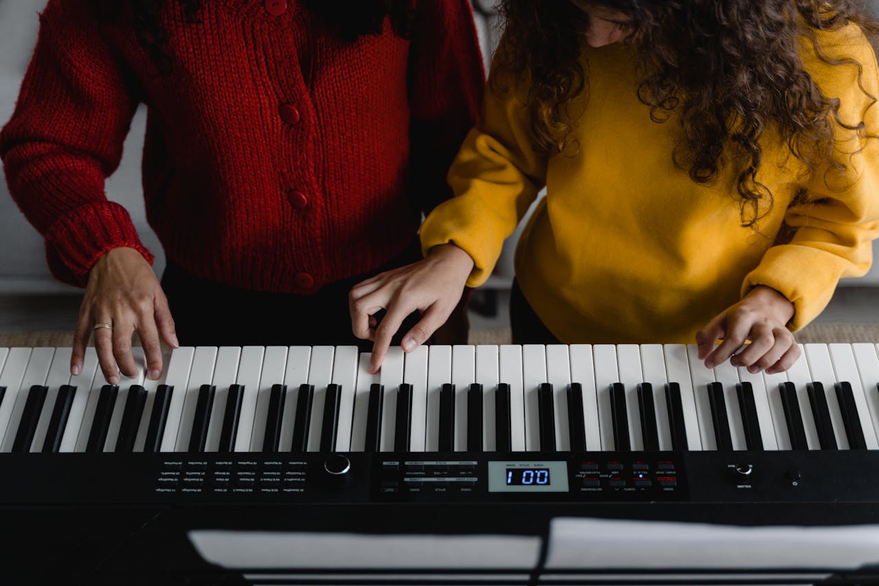 Two women playing electronic keyboard indoors. Focus on hands and instrument keys.